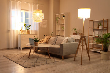 Beautiful interior of modern living room with sofa, armchair, coffee table with laptop and glowing lamps