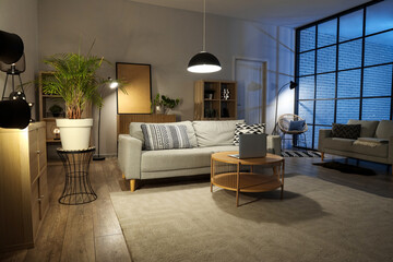 Interior of living room with comfortable sofa, table and glowing lamps