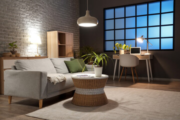 Interior of living room with comfortable sofa, tables and glowing lamps