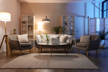 Interior of cozy living room with sofa, table, armchairs and glowing lamps