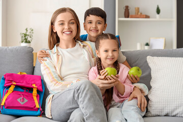 Little schoolchildren with apples and their mother sitting on sofa at home