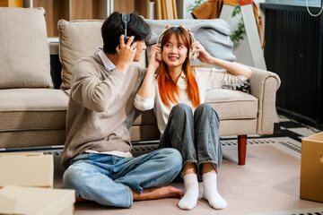 Fototapeta premium Enjoy music online with headphones in your living room. Young women, men, and Asian people find joy, dancing happily with girlfriends or boyfriends on the sofa.