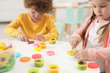 Little children modeling from plasticine at white table in kindergarten, closeup