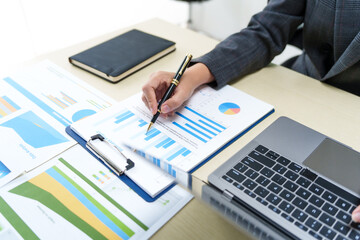 A businesswoman in a grey suit works from home, specializing in policy and planning analysis, managing financial tasks at desk with a whiteboard and expertise in accounting and financial services.