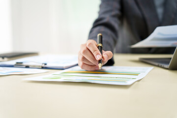 A businesswoman in a grey suit works from home, specializing in policy and planning analysis, managing financial tasks at desk with a whiteboard and expertise in accounting and financial services.