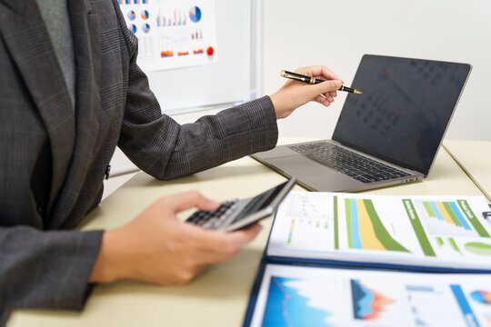A businesswoman in a grey suit works from home, specializing in policy and planning analysis, managing financial tasks at desk with a whiteboard and expertise in accounting and financial services.