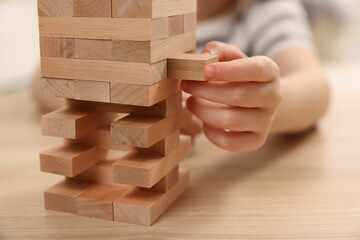 Child playing Jenga at wooden table indoors, closeup