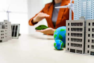 A businesswoman in a brown suit stands at a white desk with a world model, an electric car model, and a green light bulb, promoting Earth Day and sustainable green energy practices.