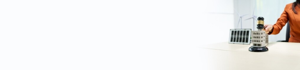 A young businesswoman is seated at a white desk, holding a lawyer's gavel. The city buildings and an electric car symbolize a commitment to green energy and sustainable policies, green car toy model.