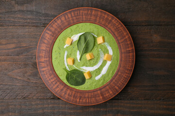 Delicious spinach cream soup with leaves and cheese in bowl on wooden table, top view