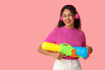 Happy African-American woman with water gun on pink background