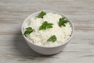 Tasty cooked rice with parsley in bowl on wooden table