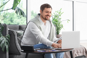 Young male teacher with laptop and notebook giving online lesson at home