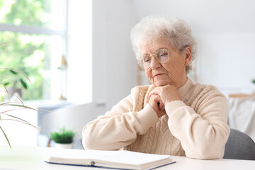 Senior woman reading Bible at table in living room