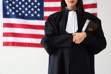 Female judge with law book against USA flag on light background, closeup. Labour Day celebration