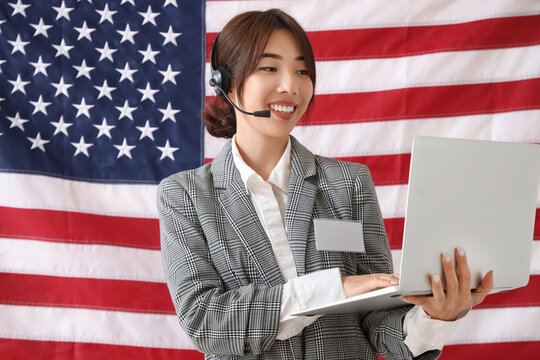 Female Asian worker in headset with laptop against USA flag. Labour Day celebration