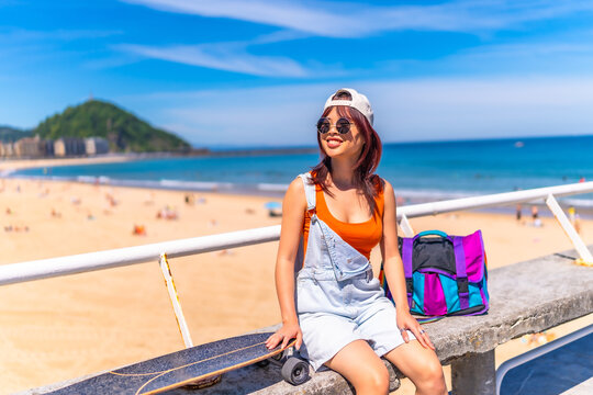 Asian woman sitting on a promenade with skateboard - Powered by Adobe