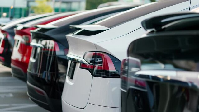 New electric vehicles lined up outdoors at modern urban vehicle car dealership, EV sedan inventory rear close-up in city dealer parking lot