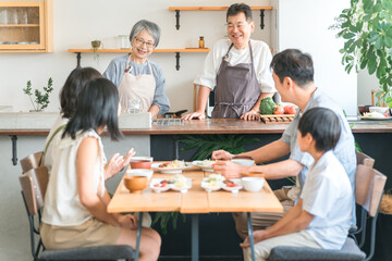 家のダイニングで家族団欒して食事する子供と夫婦・親子・三世代家族（二世帯住宅）
