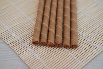 Six chocolate wafer rolls are neatly arranged in a row on a bamboo mat