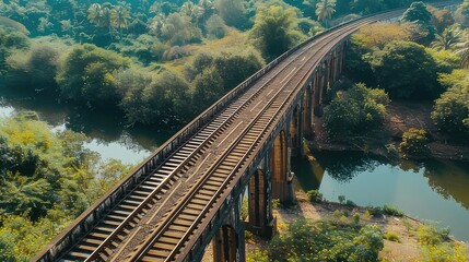 Fototapeta premium Aerial view of an old railway bridge crossing a river, surrounded by lush green trees and vegetation. Concept of travel, transportation, history, and nature.
