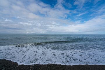 An incoming wave on the Black Sea and a pebble beach on the Sochi coast on a summer day with clouds, Sochi, Krasnodar Territory, Russia