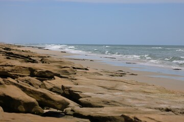 Scenic view of a rocky beach with waves crashing on the shore and a clear blue sky