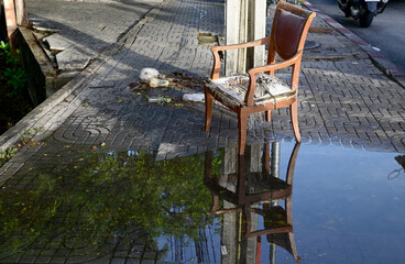 An old luxury wooden chair with only the wooden frame remaining. It was left in a pile of garbage next to an electric pole on the road in the morning at Thailand.