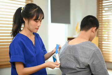 Fototapeta premium Rehabilitation specialist applying kinesio tape treatment to patient after sports muscle injury. Alternative medicine rehab