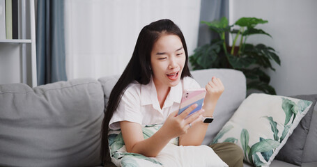 Portrait of Carefree young woman having online social chatting with her friend by smart phone on sofa at home ,Lifestyle with device technology
