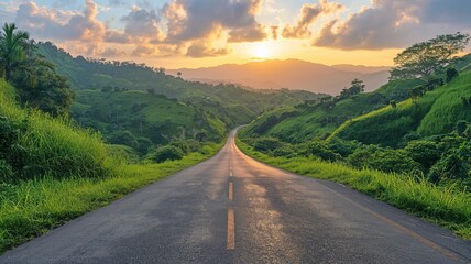 Naklejka premium A scenic road winds through lush, green hills as the sun rises, casting a warm glow over the landscape.