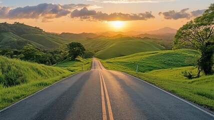 A scenic road winds through lush, green hills as the sun rises, casting a warm glow over the landscape.