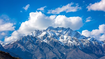 Obraz premium Snow-capped peaks with bright blue skies and white clouds.