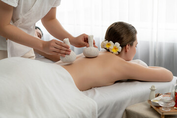 Hot herbal ball spa massage body treatment, masseur gently compresses herb bag on couple customer...