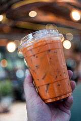 Ice Thai tea with milk in transparent plastic on man hand at coffee shop, popular menu