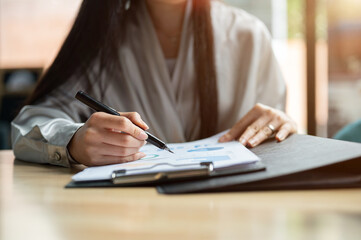 A confident, successful Asian businesswoman reviewing business reports at her desk in the office.