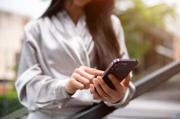 A cropped image of a businesswoman using her smartphone, replying chat while standing outdoors.