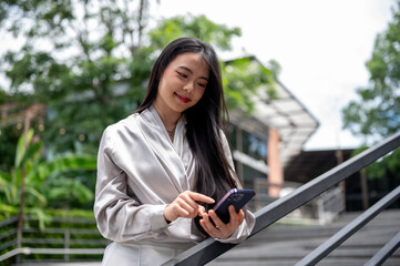 A positive Asian businesswoman is replying chat on her phone while walking down the stairs outdoors.