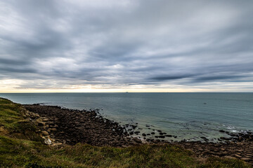 A coastal scene with rugged cliffs, cloudy sky, and serene shoreline, displaying natures beauty and peacefulness