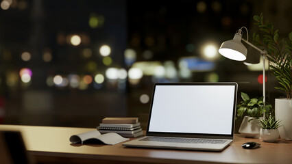 A laptop computer mockup on wooden table against the window with city nightlight view.