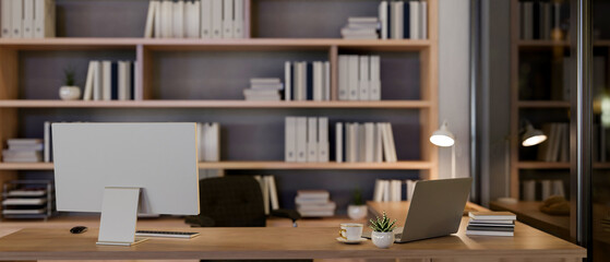 A contemporary luxurious private office at night features a computer and a laptop on a table.