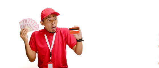 Asian delivery man holds a credit card and Indonesian Rupiah banknotes against a white background. Delivery services, financial transactions, e-commerce, and customer satisfaction.