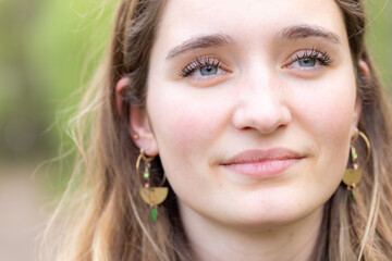 Fototapeta premium Serene portrait of a young woman with earrings, in natural outdoor light, showcasing her beauty and elegance