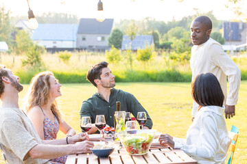 Friends having fun outdoors, enjoying wine and laughter on a sunny day in a cozy backyard dining experience