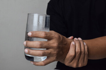 View of Man hold on hand to relief shaky symptom while drink water for parkinson's disease and chronic illness