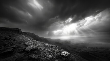 Dramatic black and white landscape depicting a stormy sky with sunlight breaking through clouds over rocky terrain, evoking a sense of awe.