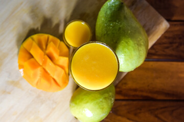 Fototapeta premium Mango juice with mango slice isolated on wooden background. Glass of tasty mango juice on table.