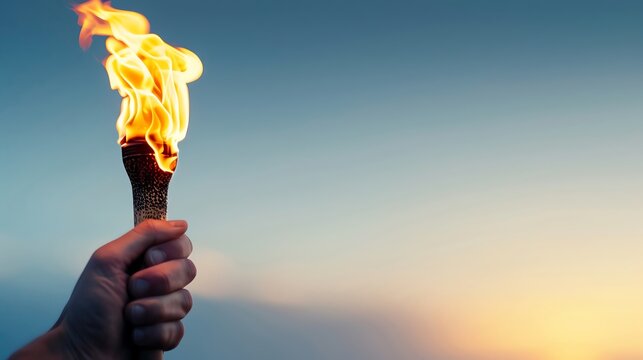 Hand holding a burning torch against a clear evening sky, symbolizing hope, leadership, achievement, and the sportspirit.