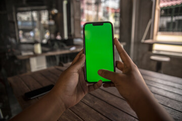 Asian woman hand holding a mobile phone with green screen at a vintage coffee shop 