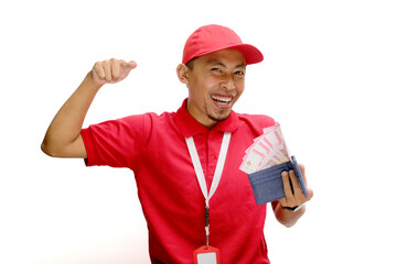 Asian delivery man or courier points towards the camera while holding money banknotes, isolated on white background. Concepts of professionalism, customer engagement, and secure monetary transactions.